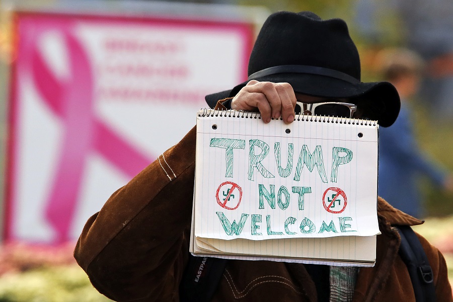 A man holds a sign outside the University of Pittsburgh's Presbyterian Hospital before the arrival of President Donald Trump's motorcade in Pittsburgh, Tuesday Oct. 30, 2018. President Trump is paying a visit to the people who were wounded Saturday, Oct. 27, 2018, when a gunman interrupted worship services at the Tree of Life Synagogue, killing 11, and wounding six. (AP Photo/Gene J. Puskar)