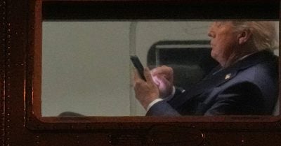 Donald Trump looking at smartphone aboard plane window during polling decline