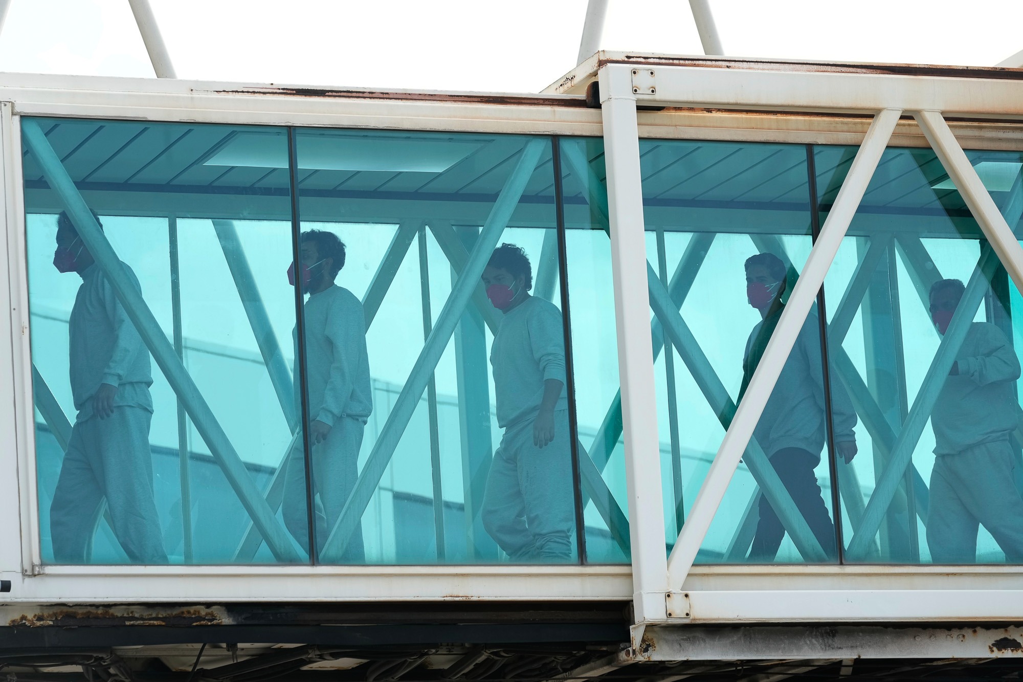 Venezuelan migrants deported from the United States wearing masks walk through a secure airport bridge after a deportation flight.