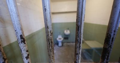 Prison cell interior seen through rusted jail bars, illustrating incarceration and prison conditions.