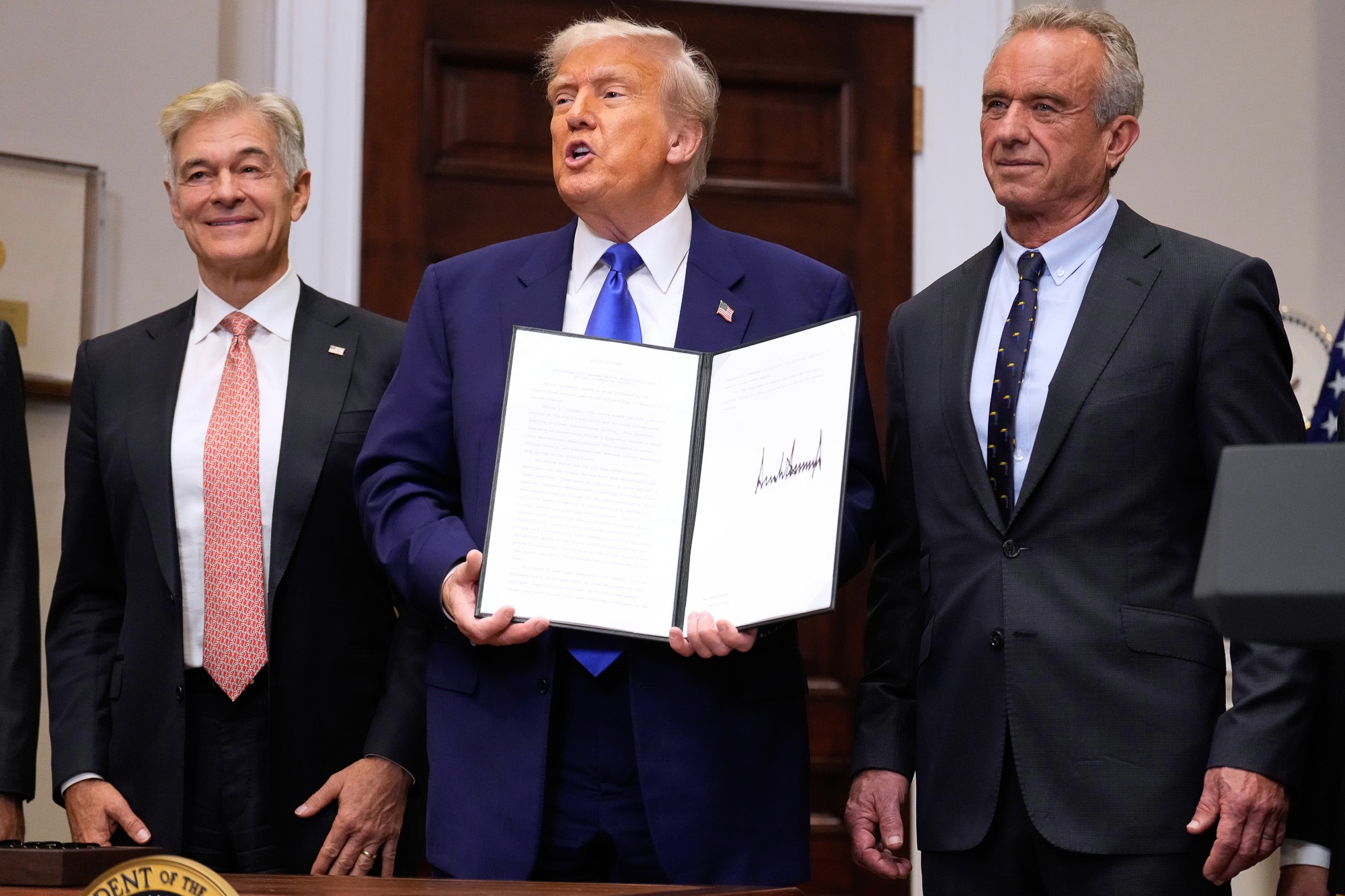 President Donald Trump, with Dr. Mehmet Oz and Robert F. Kennedy Jr., holds an executive order related to drug prices, in the Roosevelt Room of the White House.