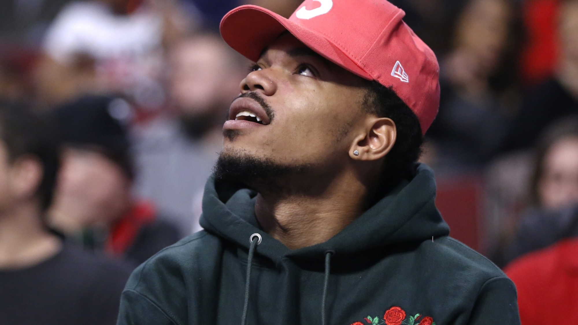 FILE- In this Feb. 24, 2017, file photo, Chance the Rapper takes watches an NBA basketball game between the Chicago Bulls and the Phoenix Suns in Chicago.  Rauner and Grammy-winning artist Chance the Rapper plan to meet this week to discuss funding education in Chicago. The performer from Chicago, whose real name is Chancelor Bennett, said Monday, Feb. 27, on Twitter that he'll meet privately with Rauner on Wednesday. (AP Photo/Charles Rex Arbogast, File)