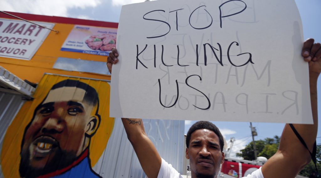 A man holds a sign in front of a mural of Alton Sterling while attorneys, not pictured, speak in front of the Triple S Food Mart in Baton Rouge, La., Thursday, July 7, 2016. Sterling, 37, was shot and killed outside the convenience store by Baton Rouge police, where he was selling CDs. (AP Photo/Gerald Herbert)
