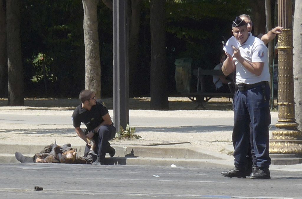 In this photo provided by Noemie Pfister, a French gendarme kneels near the dead body of a man who rammed into a police convoy and detonated an explosive device on the Champs Elysees avenue in Paris, France, Monday, June 19, 2017. Two French police officials say the man who rammed into a police convoy on Paris' Champs-Elysees was a 31-year-old man from a Paris suburb who had been flagged for extremism. (Noemie Pfister via AP)