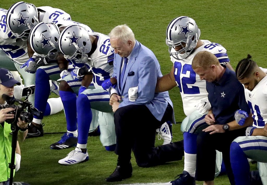 FILE - In this Monday, Sept. 25, 2017 file photo, the Dallas Cowboys, led by owner Jerry Jones, center, take a knee prior to the national anthem prior to an NFL football game against the Arizona Cardinals, in Glendale, Ariz. President Donald Trump's clash with the scores of professional football players who knelt during the Star Spangled Banner last weekend has set off a heated debate over proper etiquette during the national anthem. But throughout the world, flags, anthems and other national symbols can often divide as much as they unify, especially in countries with large religious or ethnic divisions. (AP Photo/Matt York, File)