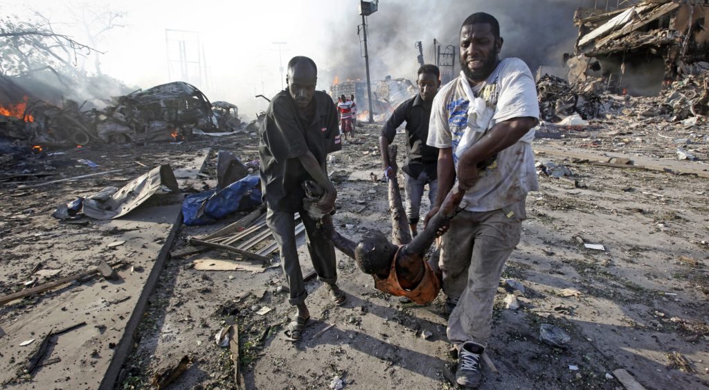 Somalis remove the body of a man killed in a blast in the capital Mogadishu, Somalia Saturday, Oct. 14, 2017. A huge explosion from a truck bomb has killed at least 20 people in Somalia's capital, police said Saturday, as shaken residents called it the most powerful blast they'd heard in years. (AP Photo/Farah Abdi Warsameh)