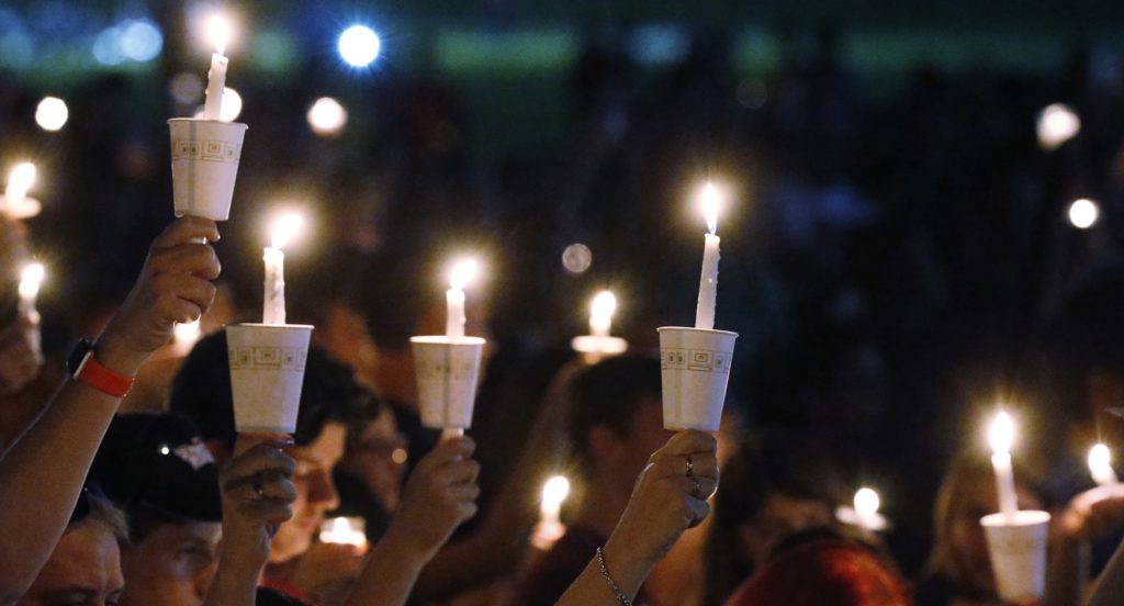 Attendees raise their candles at a candlelight vigil for the victims of the shooting at Marjory Stoneman Douglas High School, Thursday, Feb. 15, 2018, in Parkland, Fla. The teenager accused of using a semi-automatic rifle to kill more than a dozen people and injuring others at a Florida high school confessed to carrying out one of the nation's deadliest school shootings and concealing extra ammunition in his backpack, according to a sheriff's department report released Thursday. (AP Photo/Wilfredo Lee)