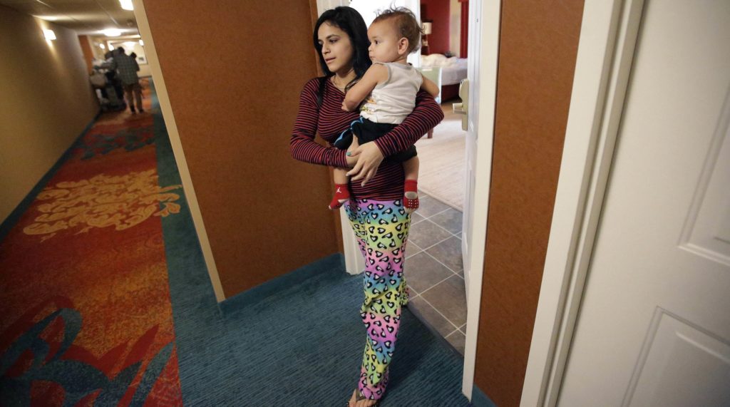 In this Tuesday, Feb. 27, 2018 photo, Jesenia Flores, 19, holds her son Jose, both of Aibonito, Puerto Rico, as she steps out of her hotel room, in Dedham, Mass. The hotel initially offered a welcome break from the chaos after the storm. But now it's become tedious. "The only entertainment I have is my son," she said. (AP Photo/Steven Senne)
