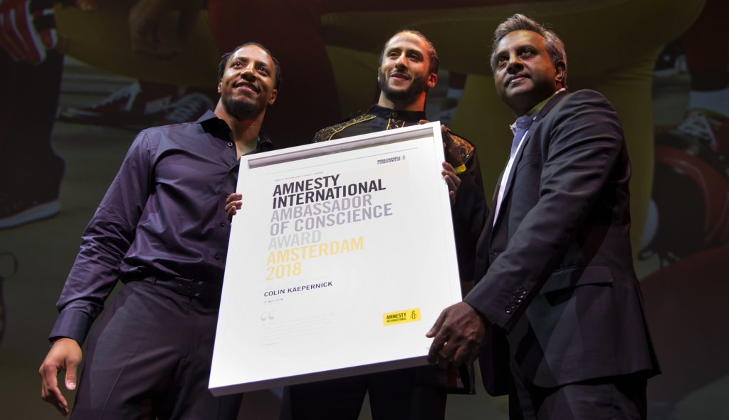 Former NFL quarterback and social justice activist Colin Kaepernick receives the Amnesty International Ambassador of Conscience Award for 2018 from Amnesty International Secretary General Salil Shetty, right, and colleague Eric Reid, left, in Amsterdam, Saturday April 21, 2018. Kaepernick became a controversial figure when refusing to stand for the national anthem, instead he knelt to protest racial inequality and police brutality. (AP Photo/Peter Dejong)