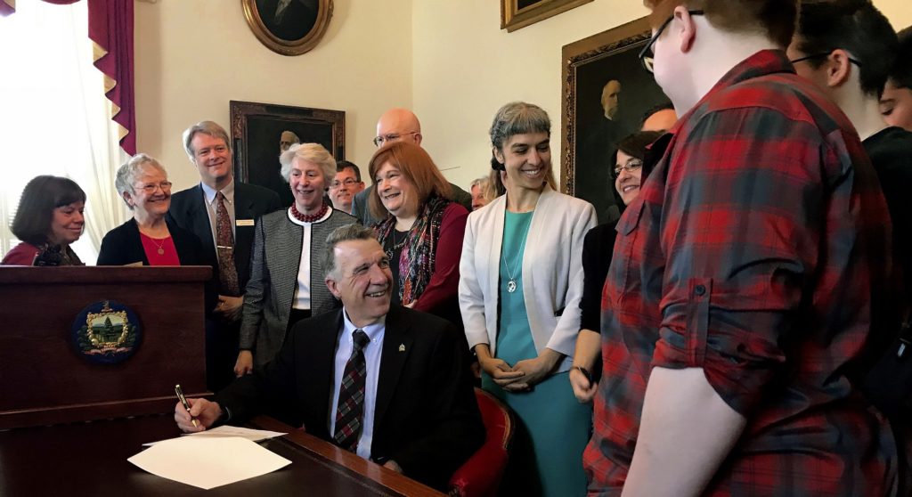 Gov. Phil Scott, seated, smiles after signing a bill requiring that all single occupancy restrooms in Vermont public buildings be marked as gender neutral, Friday, May 11, 2018 in Montpelier, Vt.,  The new law takes effect July 1. (AP Photo/David Jordan)