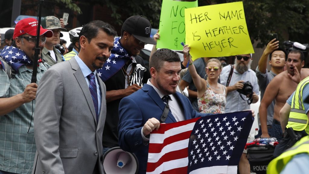 White nationalist Jason Kessler, center, walks to the White House to rally on the one year anniversary of the Charlottesville "Unite the Right" rally, Sunday, Aug. 12, 2018, in Washington. In the background is a protester holding a sign referencing the woman that died in last year's rally that says, "her name is Heather Heyer." (AP Photo/Jacquelyn Martin)