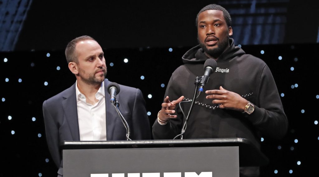 Philadelphia 76ers co-owner and Fanatics executive Michael Rubin, left, listens as recordng artist Meek Mill speaks at the launch of a partnership of sports, business and recording artists who hope to transform the American criminal justice system, Wednesday, Jan. 23, 2019, in New York. (AP Photo/Kathy Willens)