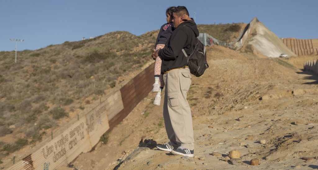 A migrant from Honduras holds his daughter as they look towards the U.S. before they jump the border fence to get into the U.S. side to San Diego, Calif., from Tijuana, Mexico, Thursday, Jan. 3, 2019. Discouraged by the long wait to apply for asylum through official ports of entry, many migrants from recent caravans are choosing to cross the U.S. border wall and hand themselves in to border patrol agents. (AP Photo/Daniel Ochoa de Olza)