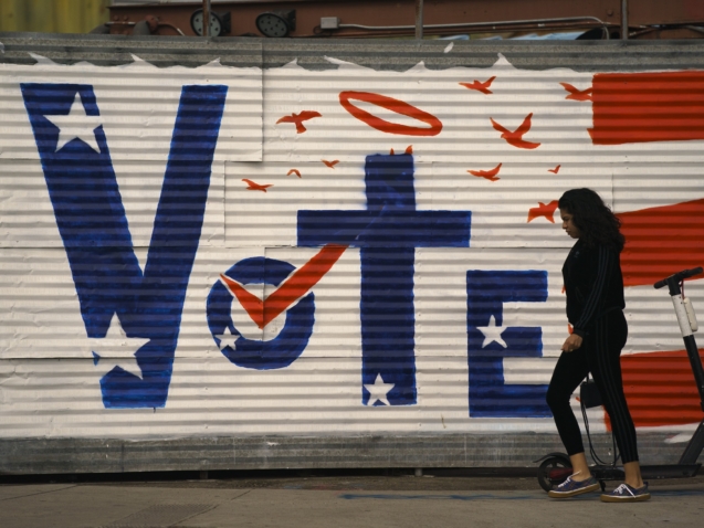 A woman walks past a voting sign painted on a wall Monday, Nov. 2, 2020, in the Venice Beach section of Los Angeles. (AP Photo/Jae C. Hong)