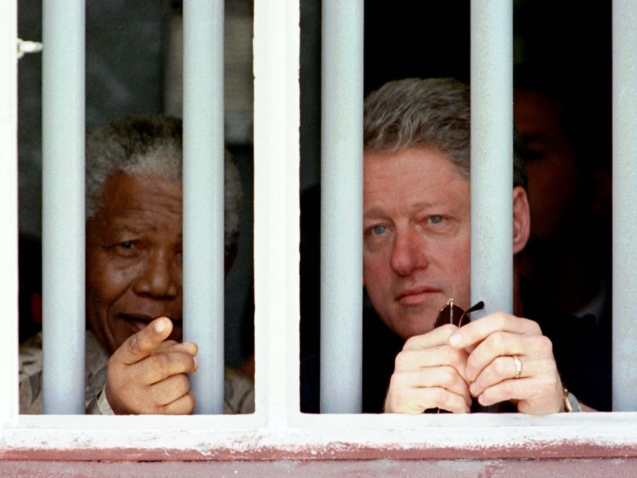 FILE - In this March 27, 1998 file photo, South African President Nelson Mandela, left, and U.S. President Bill Clinton peer through the bars of prison cell No. 5, the cramped, gray cell where Mandela was jailed for 18 years in his struggle against apartheid, on Robben Island, South Africa.  South Africa's president Jacob Zuma says, Thursday, Dec. 5, 2013, that Mandela has died. He was 95.   (AP Photo/Rick Wilking, Pool)