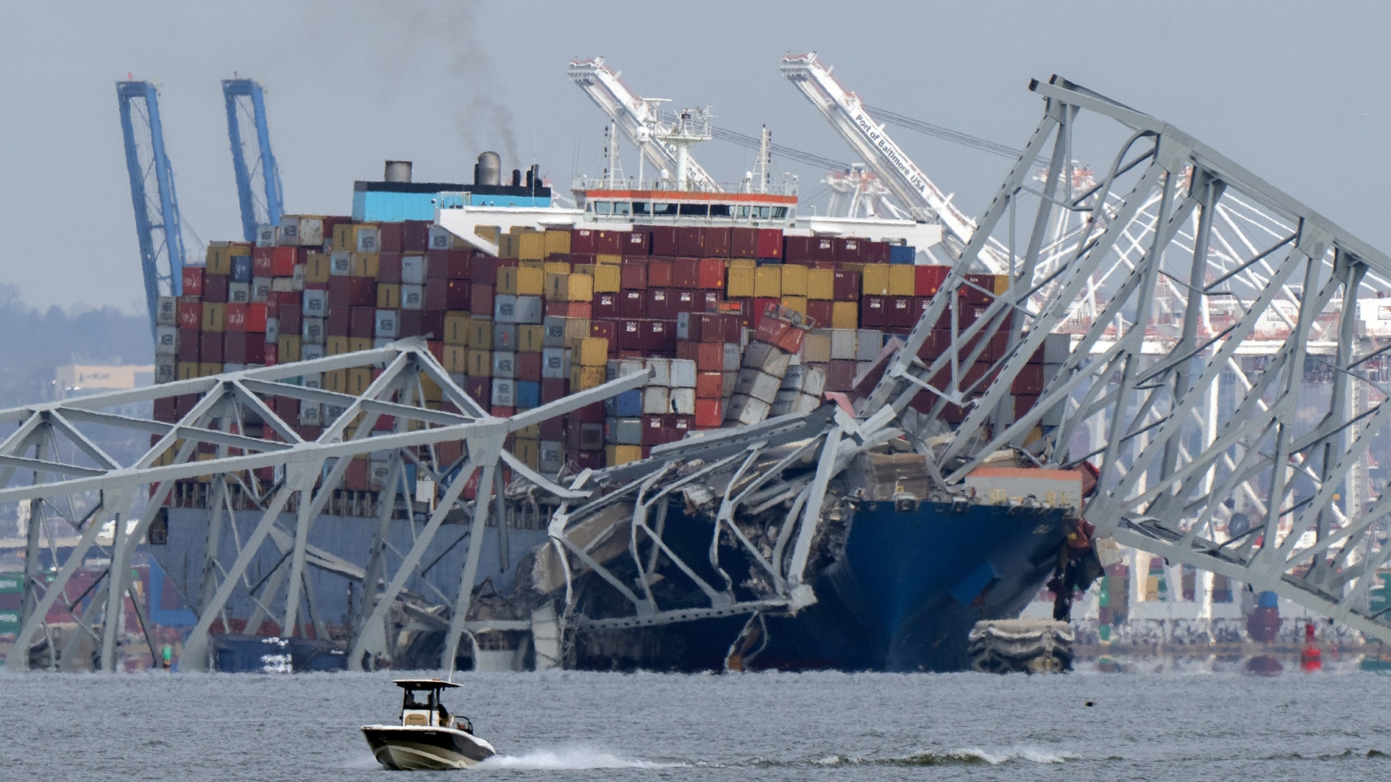 A boat moves past a container ship as it rests against wreckage of the Francis Scott Key Bridge on Tuesday, March 26, 2024, as seen from Pasadena, Md. The container ship lost power and rammed into the major bridge in Baltimore early Tuesday, causing it to snap and plunge into the river below. Several vehicles fell into the chilly waters, and rescuers searched for survivors. (AP Photo/Mark Schiefelbein)