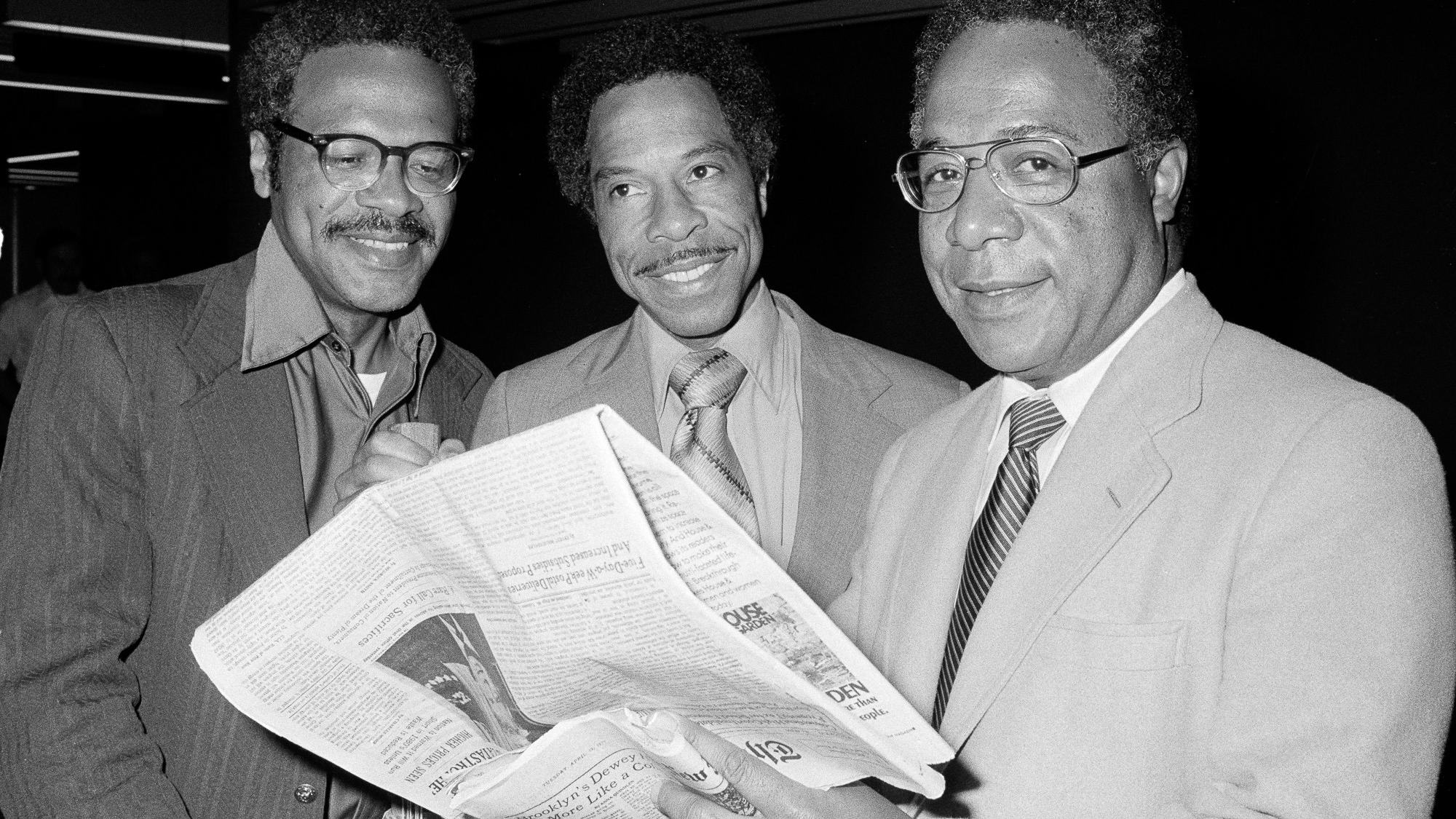Author Alex Haley, right, poses with his brothers Julius, left, and George, at John F. Kennedy Airport in New York, April 19, 1977, after their return from the African village of Juffre in Gambia, where Alex had traced an ancestor for his book "Roots." Haley was surprised by an article in the newspaper he's holding claiming that he was awarded a special Pulitzer Prize for his best-selling book. (AP Photo/Ira Schwarz)