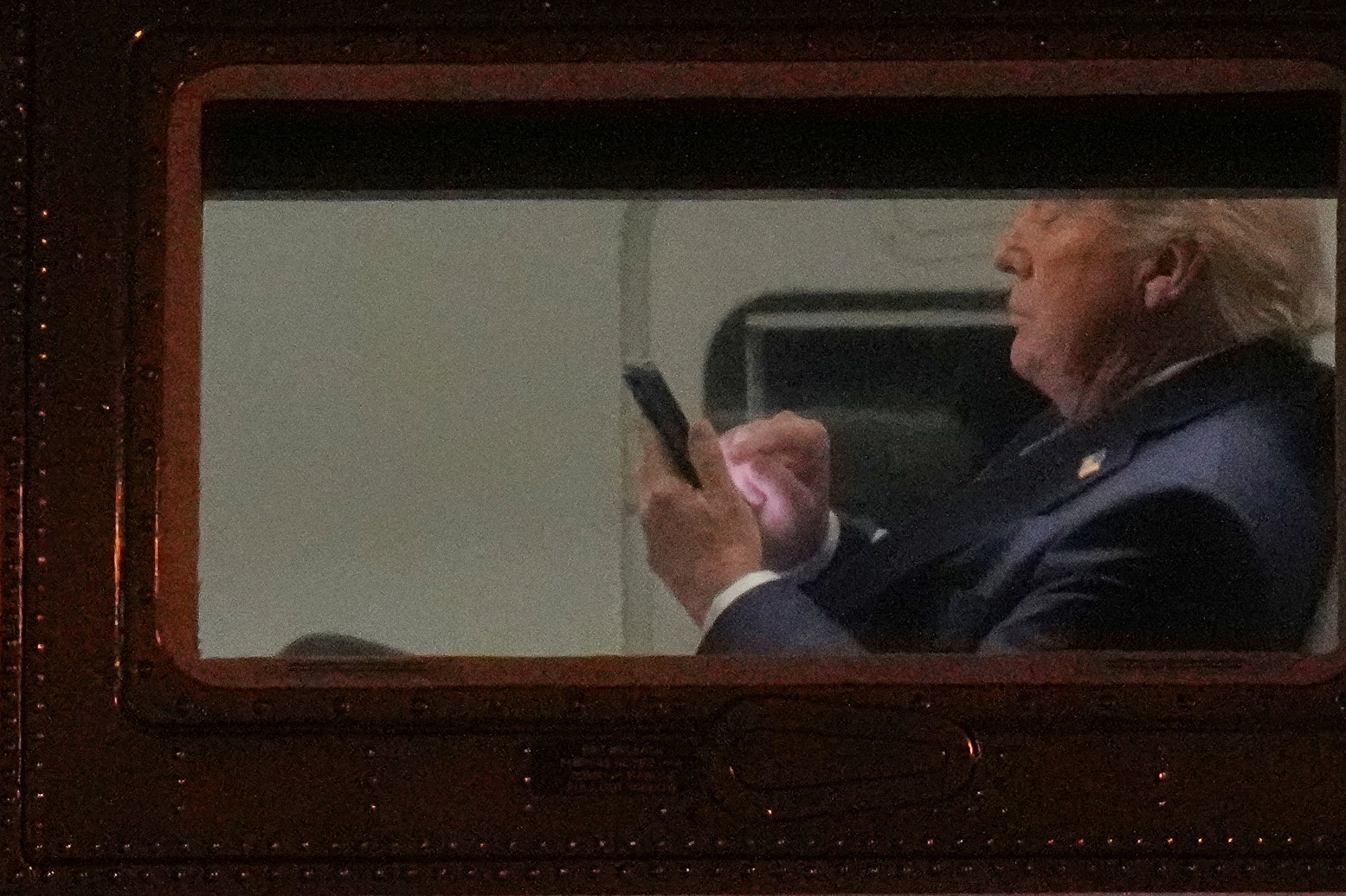 Donald Trump looking at smartphone aboard plane window during polling decline