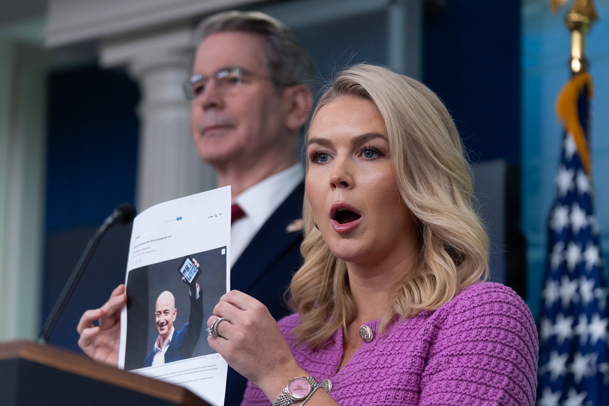 White House Press Secretary Karoline Leavitt holds a printed photo of Jeff Bezos while addressing the media about Amazon and tariff-related controversy.