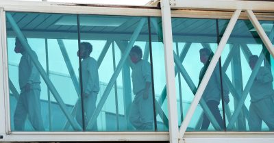 Venezuelan migrants deported from the United States wearing masks walk through a secure airport bridge after a deportation flight.