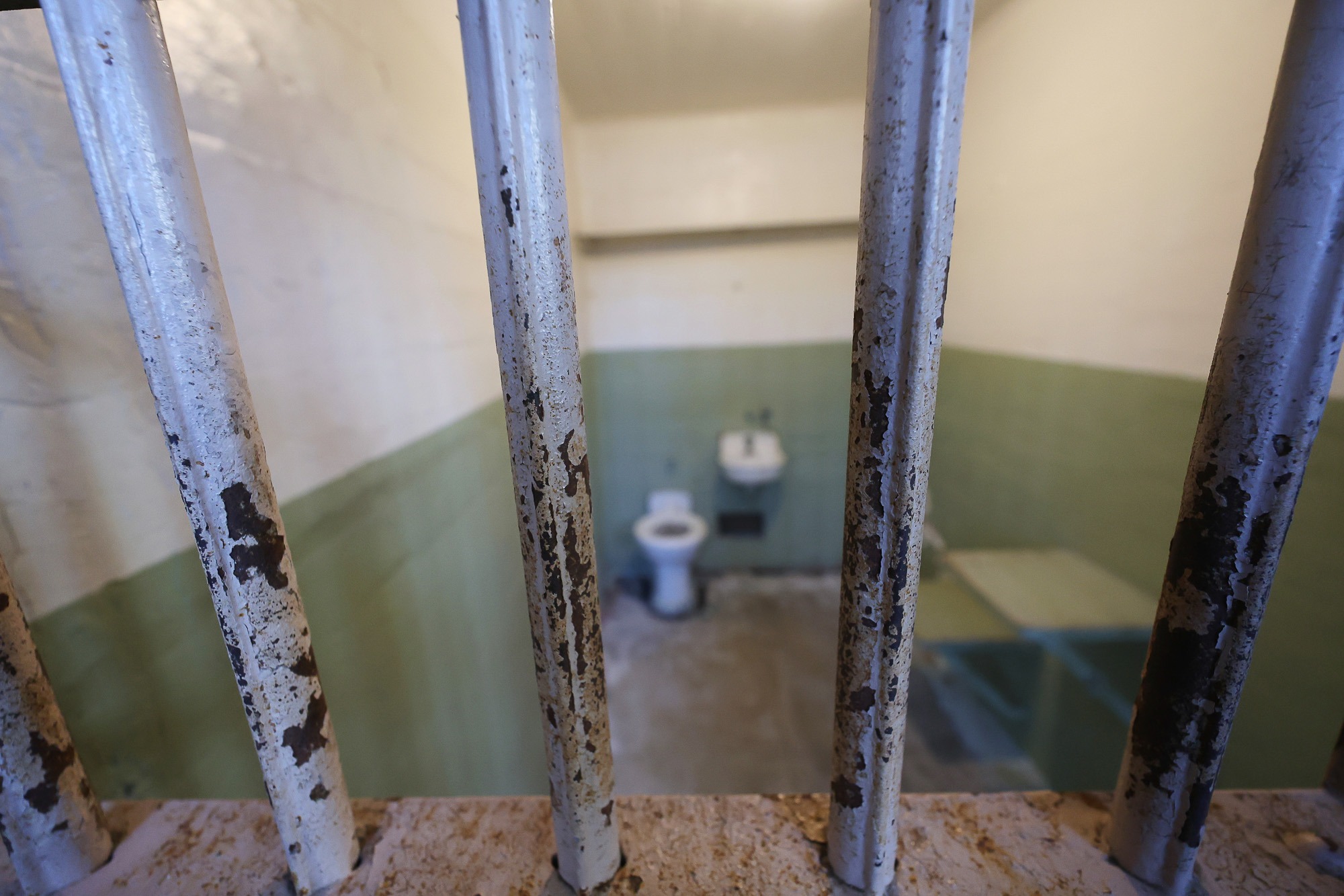 Prison cell interior seen through rusted jail bars, illustrating incarceration and prison conditions.